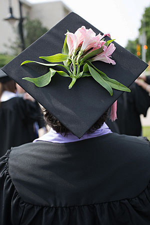 A graduating student in cap and gown with a flower on her mortar board