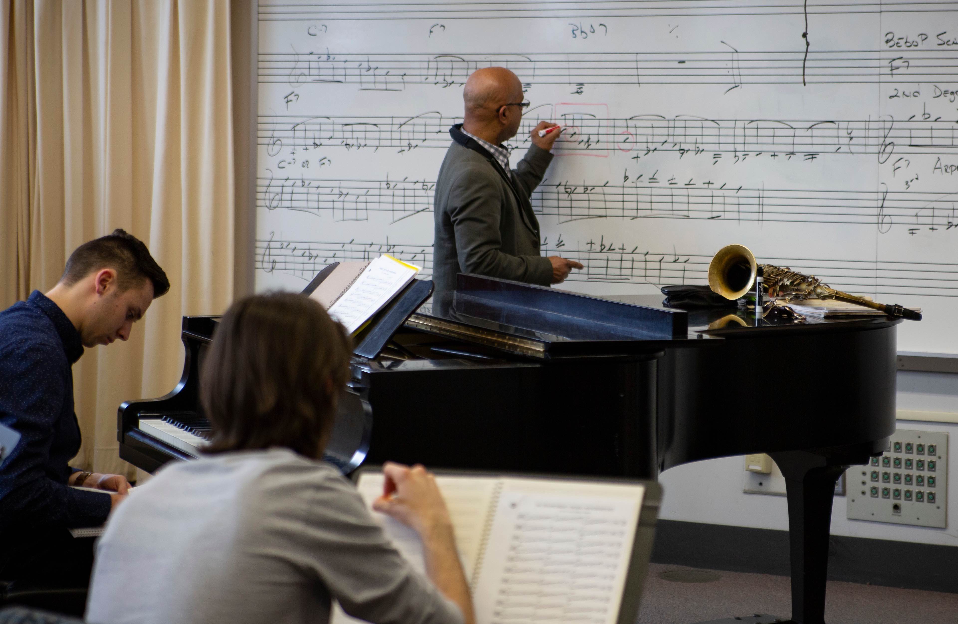 Director of Jazz Studies Jose Encarnacion writing musical notations on whiteboard.